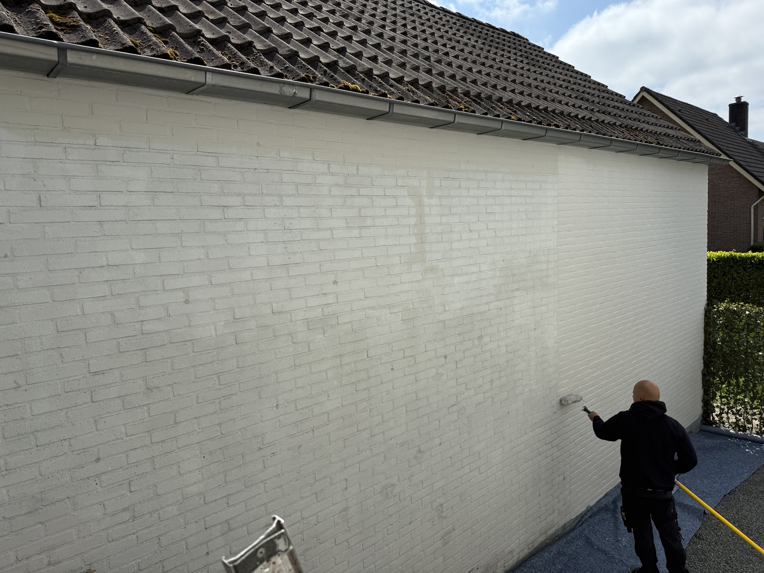Schilder brengt witte muurverf aan op een buitengevel